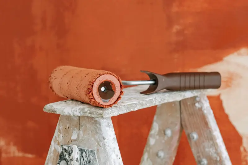 Verfroller met terracotta verf op een trapladder voor een wand die half in de nieuwe kleur staat